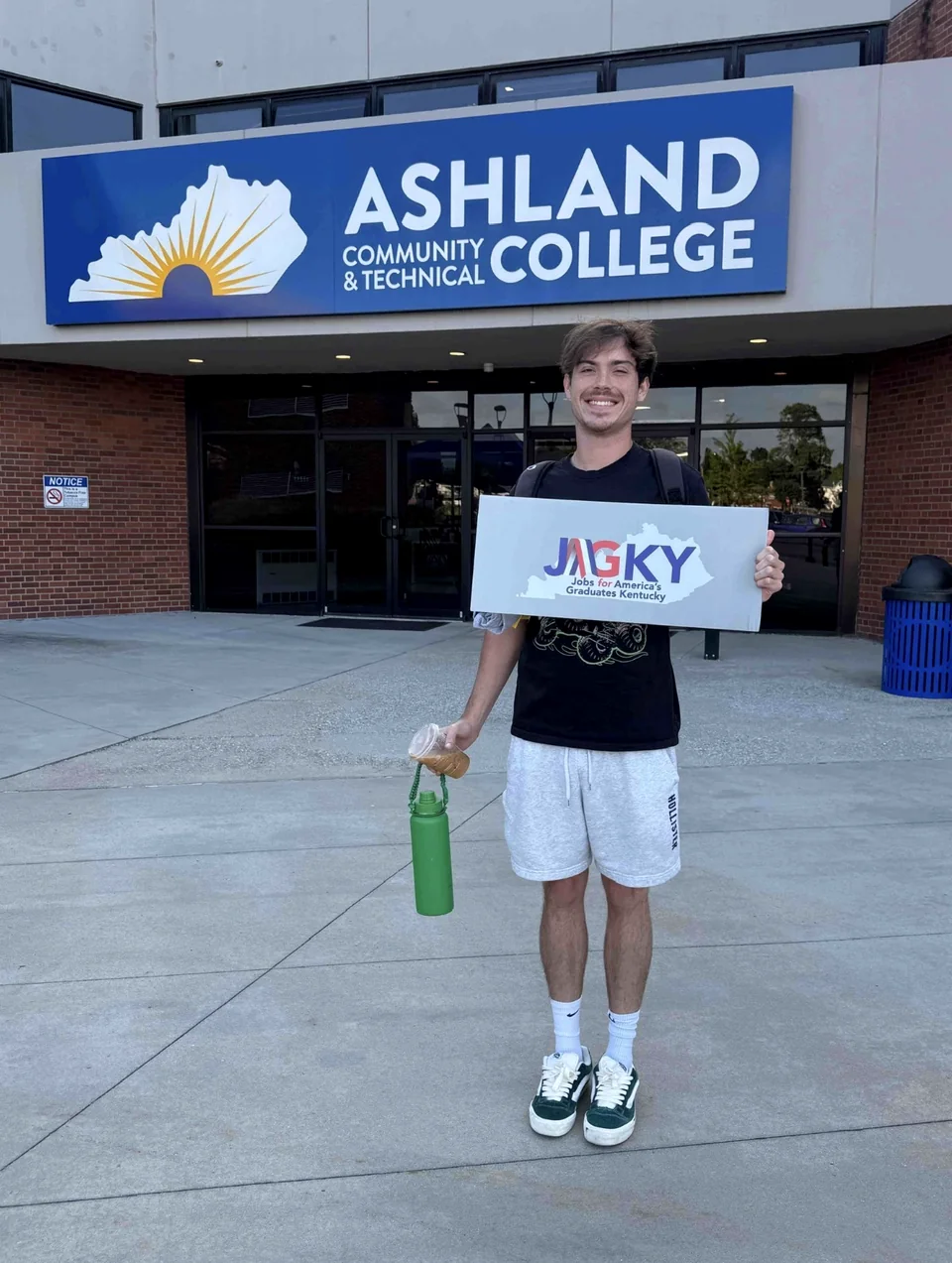 Hunter holding a JAG Kentucky sign in front of Ashland Community and Technical College.